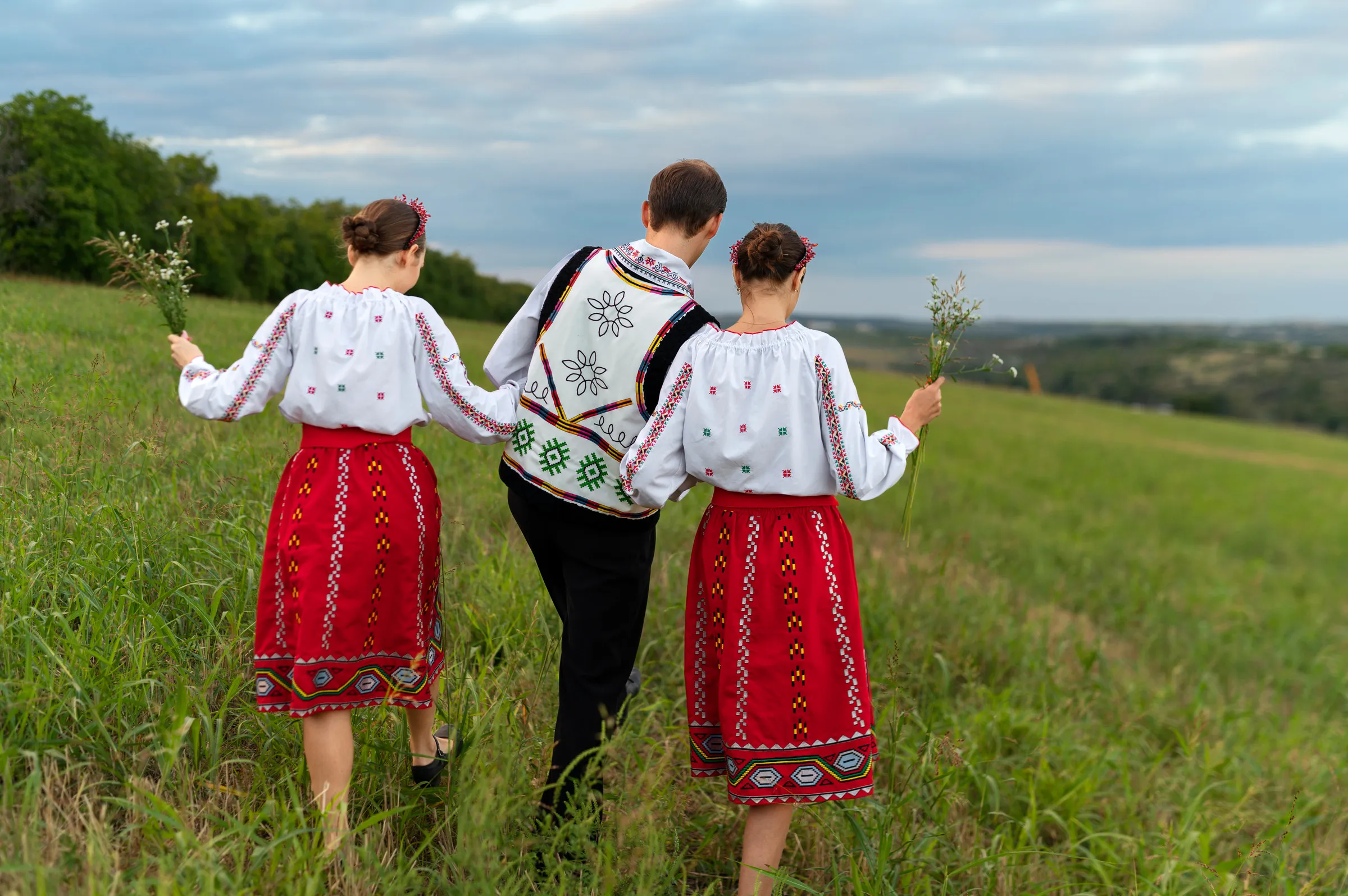 Three people in traditional embroidered folk costumes walking through a meadow