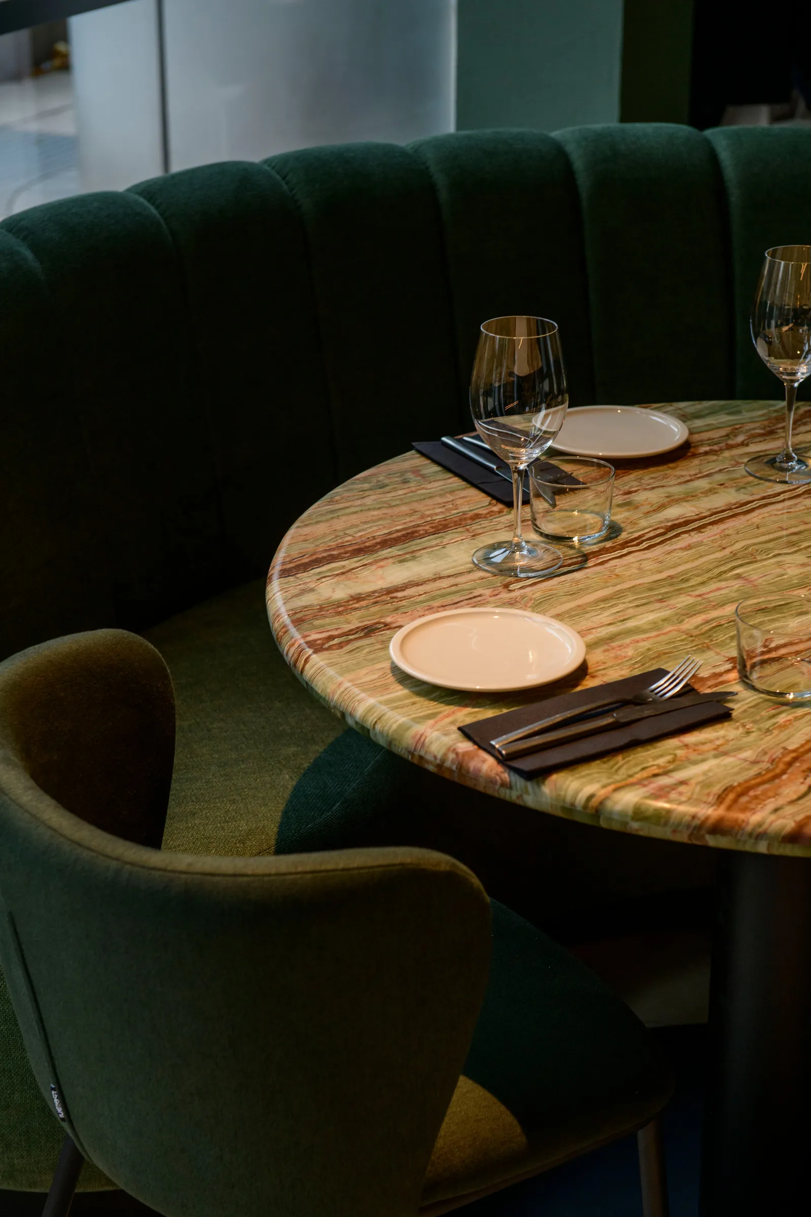 Round onyx table set for dinner beside a green velvet booth