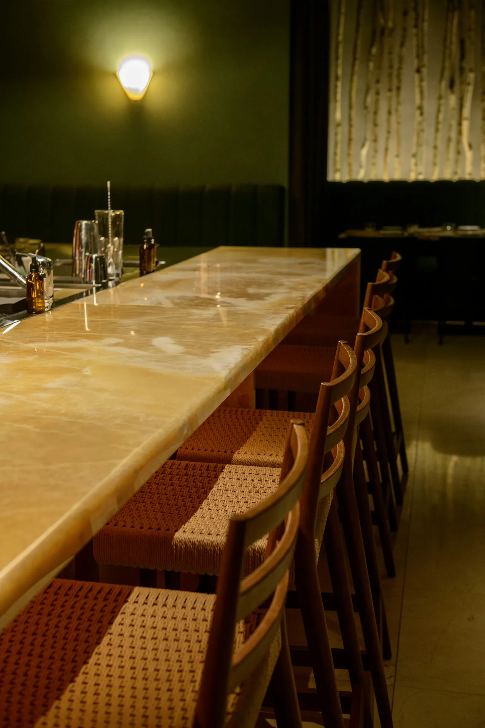 Long backlit onyx bar counter with woven bar stools