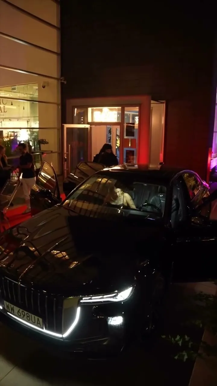 Czarna limuzyna Hongqi z zapalonymi światłami przed wejściem do restauracji