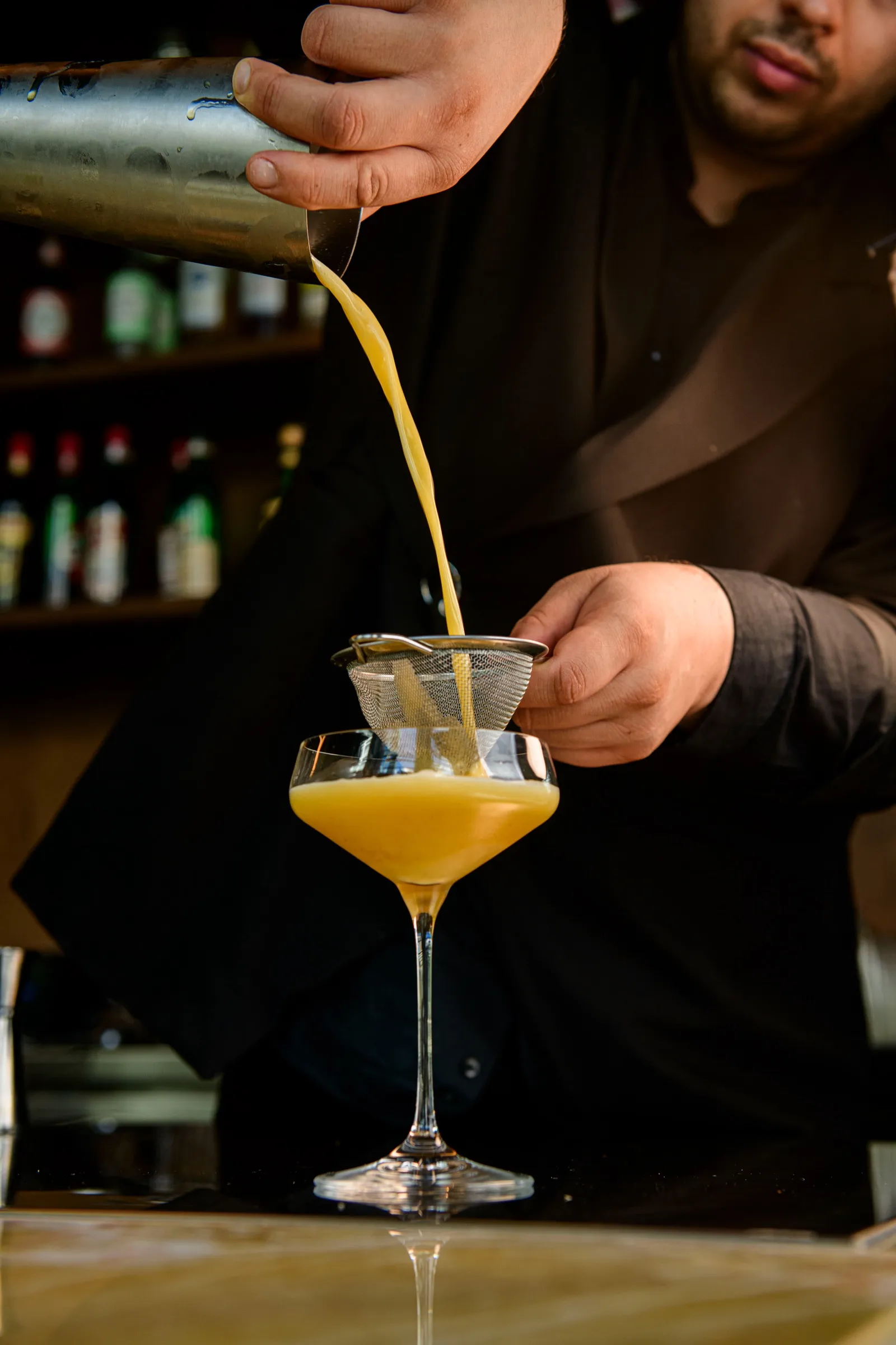 Barman przecedza pomarańczowy koktajl do kieliszka coupe