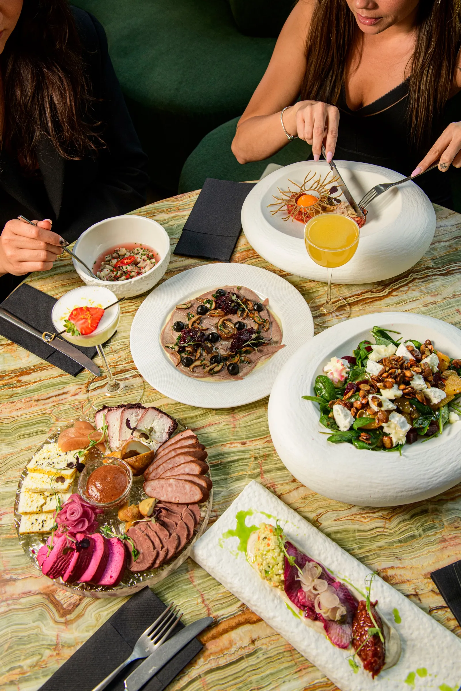 Guests sharing starters, salads and a cold cuts platter around a round onyx table